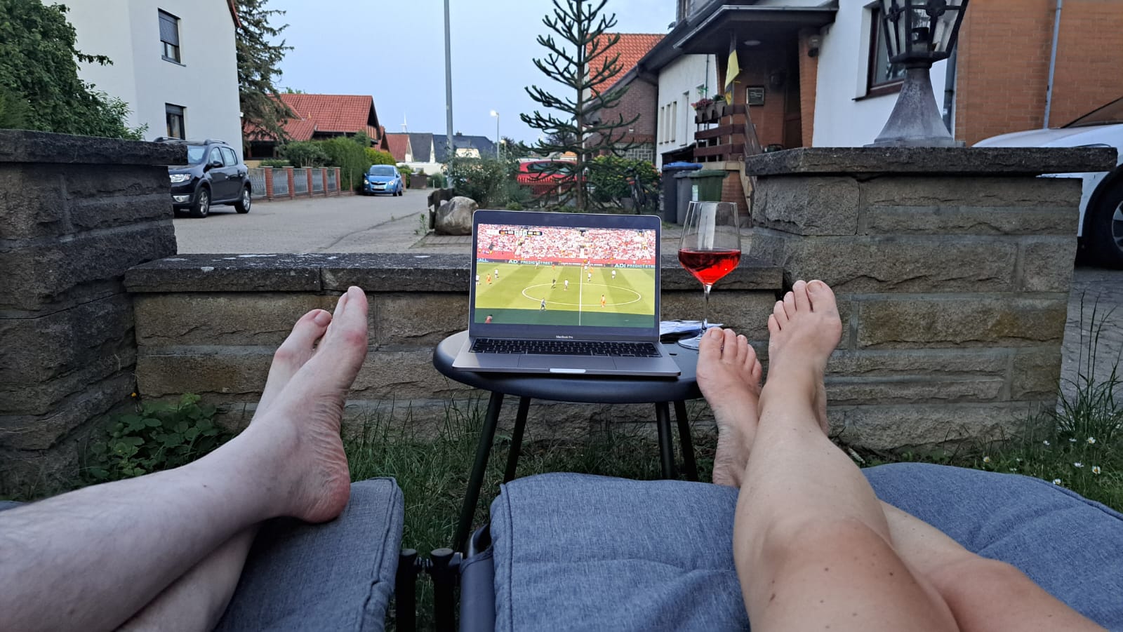 Fußball-WM auf einem Laptop im Vorgarten, gesehen von zwei Liegen mit hochgelegten Füßen